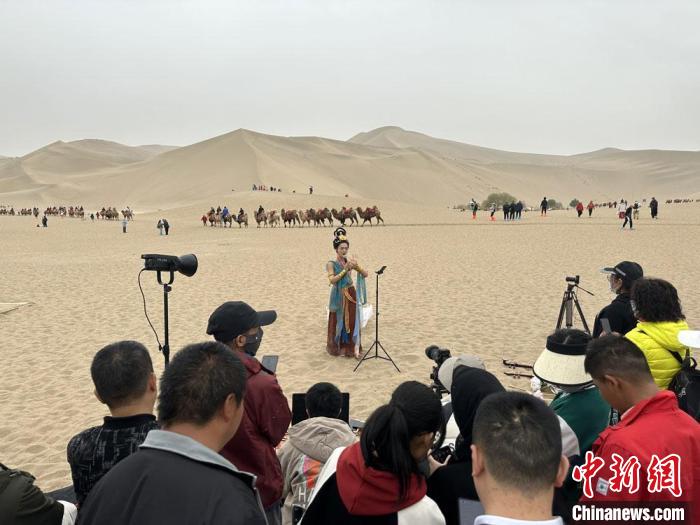 圖為2023年4月底，敦煌大漠“逐舞者”奧楠在鳴沙山月牙泉景區(qū)視頻直播，吸引游人圍觀(guān)?！●T志軍 攝