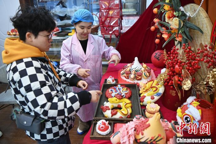 1月25日，隨著春節(jié)臨近，蘭州一花饃店“龍”元素花饃熱銷。圖為工作人員向顧客推薦“龍”元素花饃。九美旦增 攝</p><p>